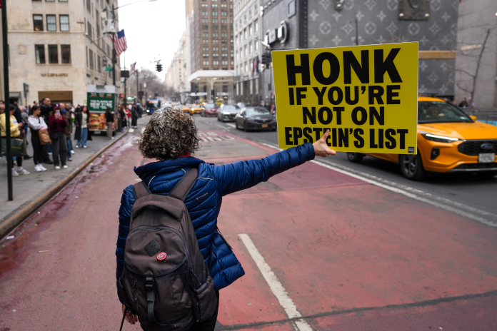 "Klaxonnez si vous n'êtes pas sur la liste d'Epstein" proclame le panneau brandi par une militante féministe à New York, au pied de la Trump Tower, le 8 mars 2026 (photo Ryan Murphy/AFP).