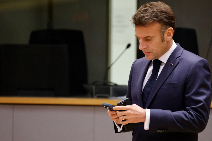 Emmanuel Macron consultant ses deux téléphones en marge d'une réunion à Bruxelles, en mars 2025 (photo Ludovic Marin/AFP).