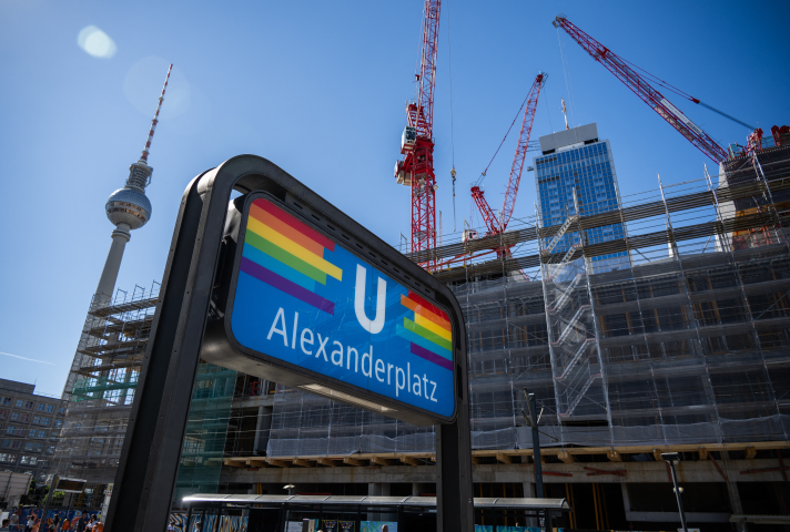 Une enseigne de station de métro est décorée d'un drapeau arc-en-ciel devant le gratte-ciel en construction du géant immobilier français Covivio à Alexanderplatz, à Berlin, le 21 août 2025. (Photo de John MACDOUGALL / AFP)